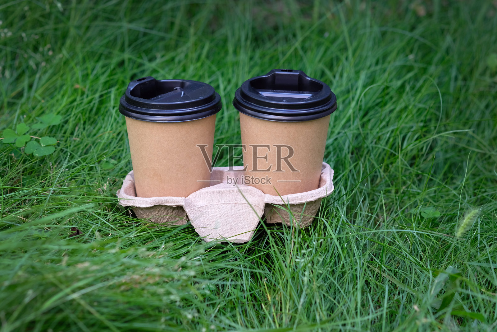 两个带黑色盖子的棕色纸杯，放在草地的背景下。照片摄影图片