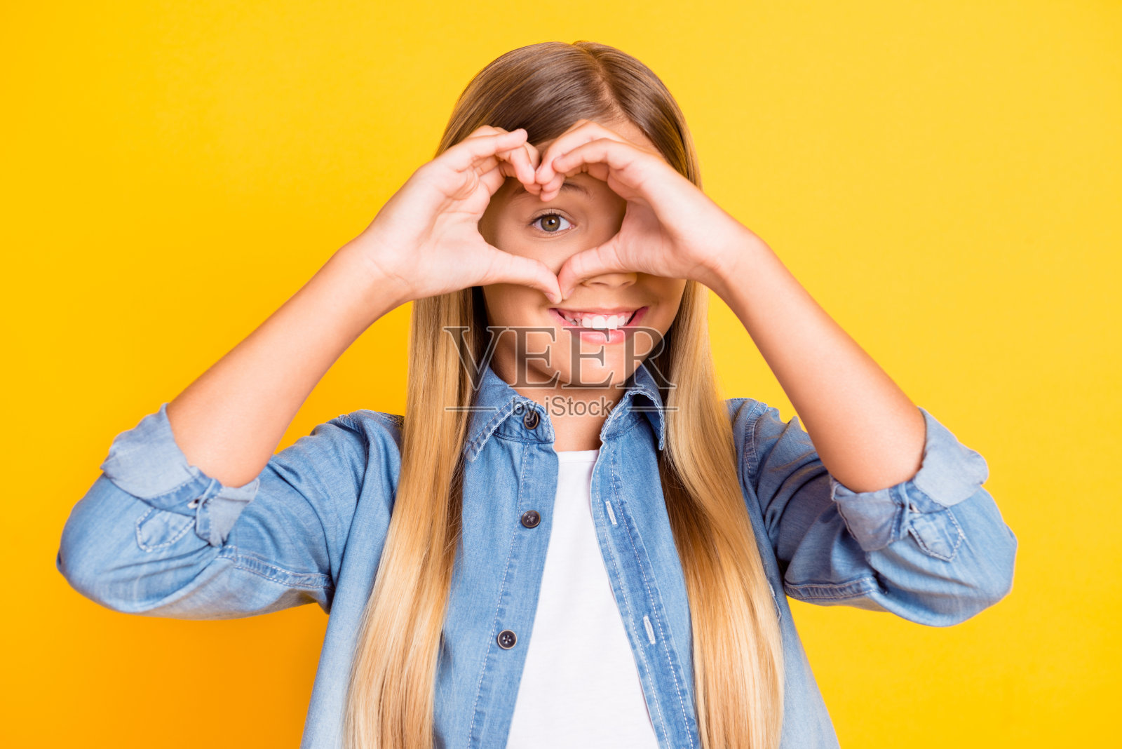 照片肖像的漂亮的女学生显示心与她的手看扔穿着牛仔衬衫微笑孤立在明亮的黄色背景照片摄影图片