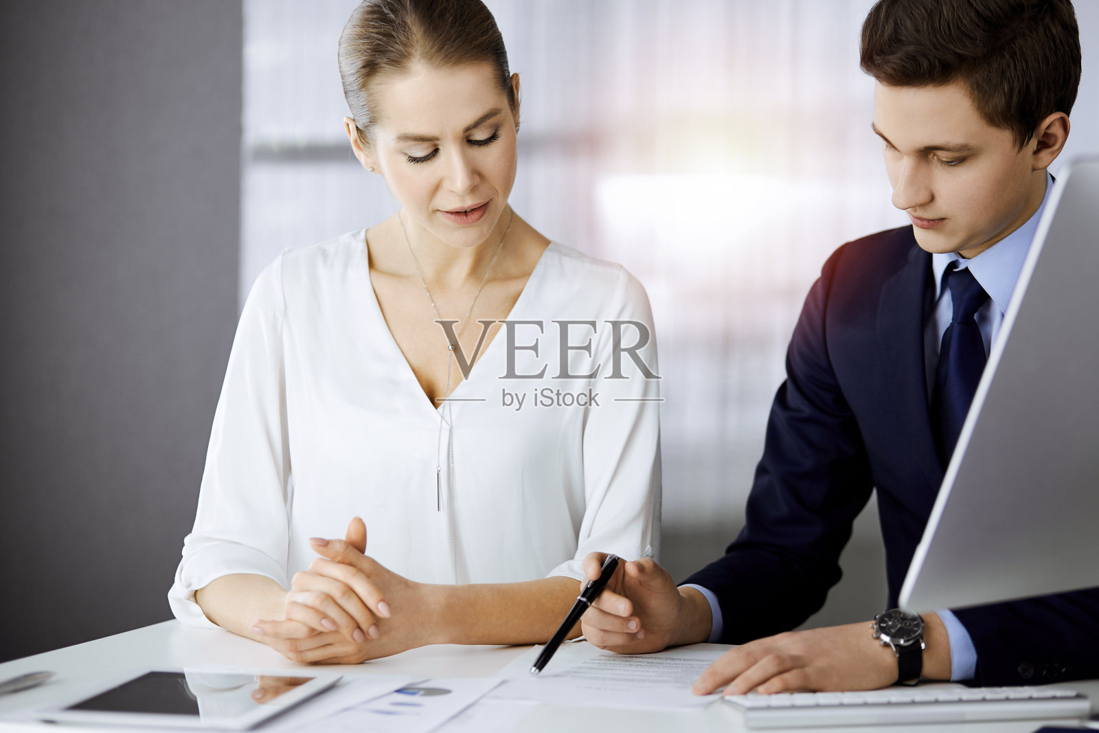 商务人士坐在阳光明媚的办公室里讨论某事。在和男同事交谈时，专注于女商人照片摄影图片