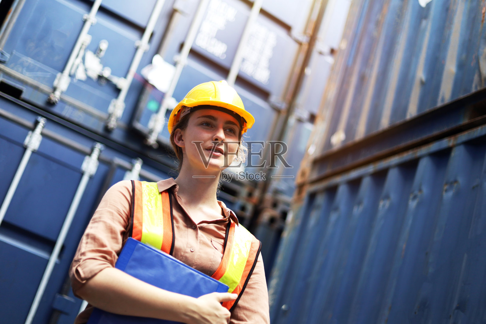 年轻的女工程师站在船坞跟踪货物库存和检查集装箱箱子的安全。照片摄影图片