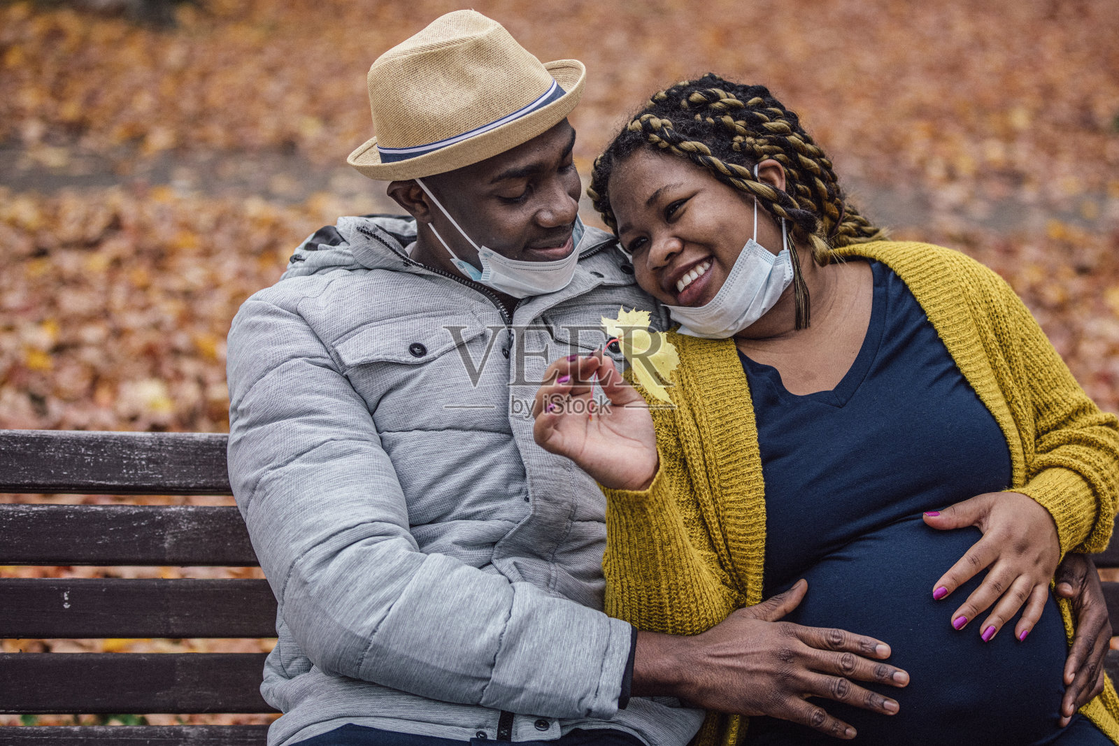 在一个秋高气爽的日子里，一对戴着防护口罩的夫妇坐在公园的长椅上休息。照片摄影图片