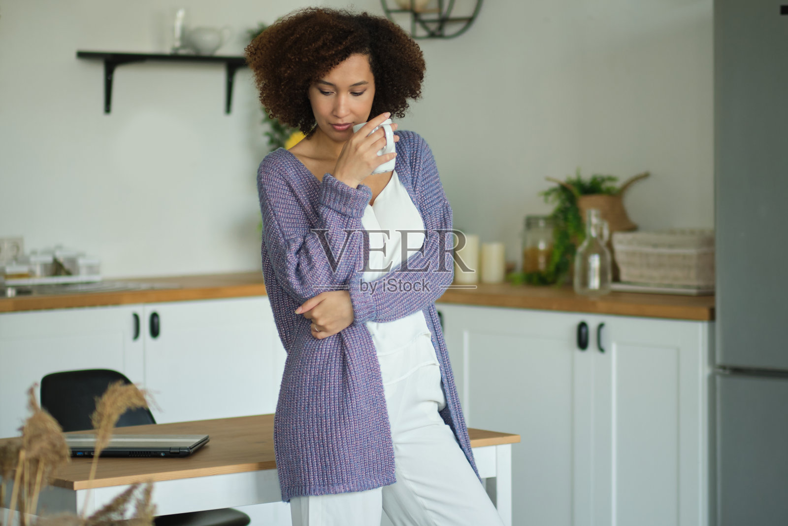 在厨房里端着一杯咖啡的快乐女人。年轻的非洲裔美国女性在喝咖啡照片摄影图片