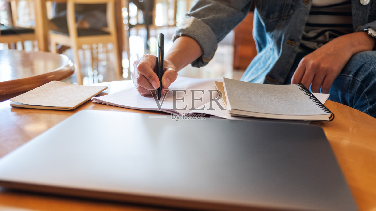 一个女人在笔记本上写字，桌上放着一台笔记本电脑照片摄影图片