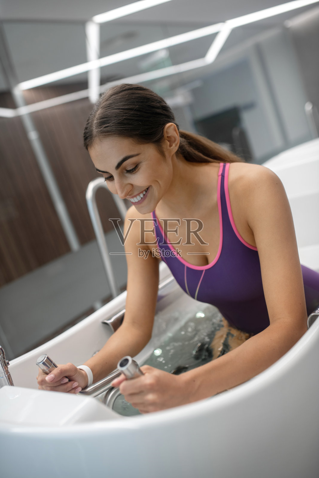 兴奋的黑发女性在紫色泳衣有水按摩照片摄影图片