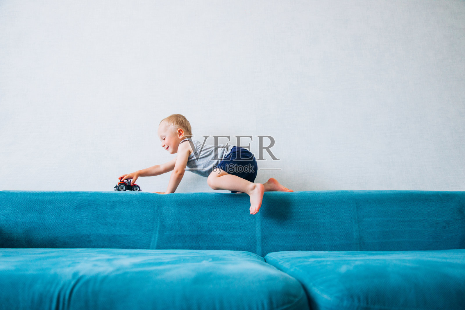 一个小男孩在沙发上玩玩具车。照片摄影图片