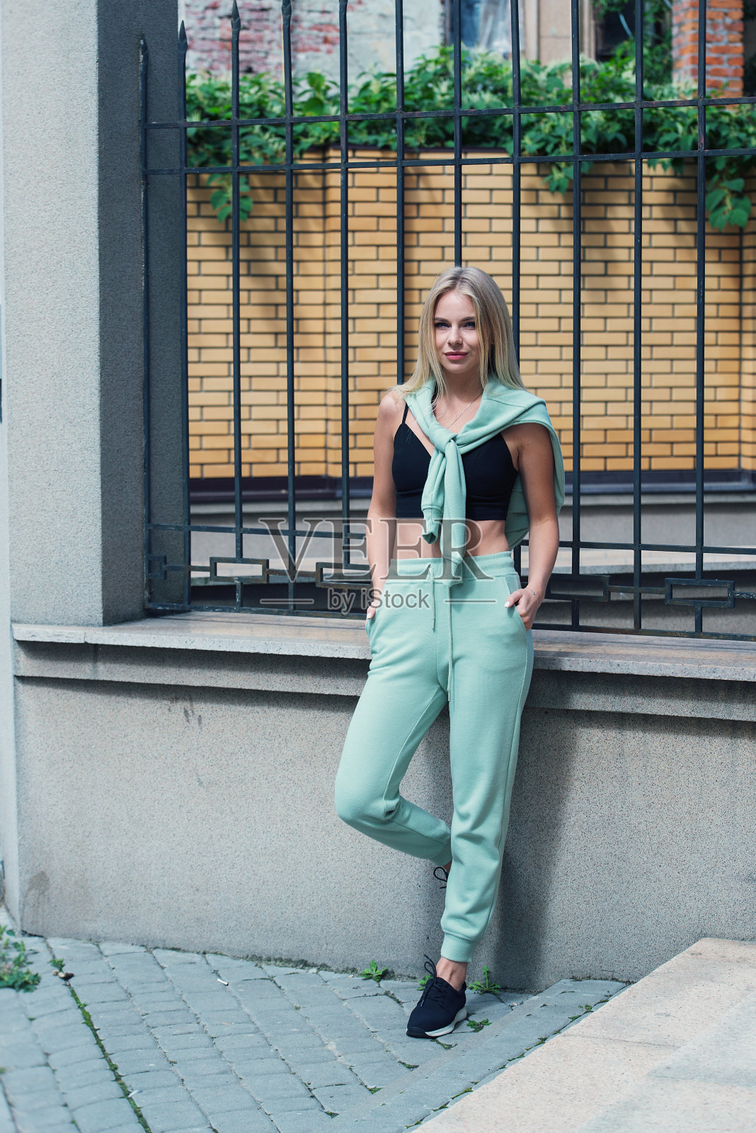 时髦漂亮的年轻女人在淡绿色运动服摆姿势在街上。迷人的女孩模特在户外摆姿势照片摄影图片
