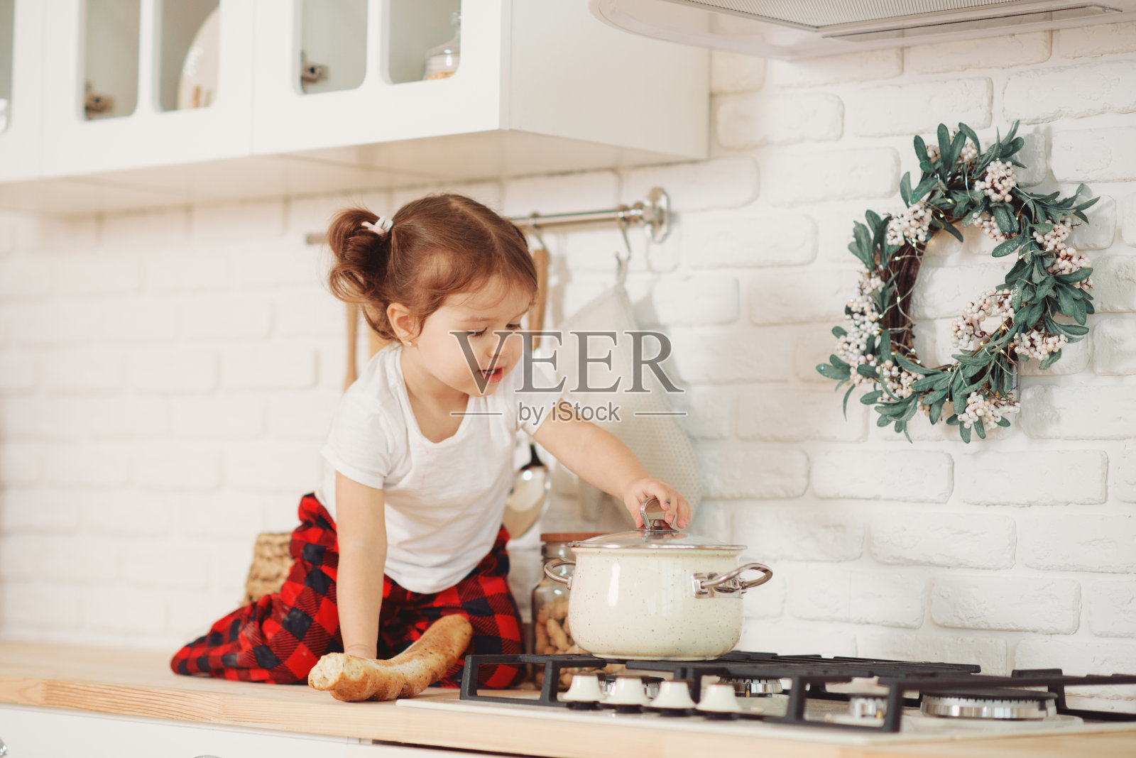 可爱的小女孩戴着圣诞帽，在家厨房准备饼干。坐在厨房的桌子上，帮助妈妈准备节日的圣诞晚餐照片摄影图片