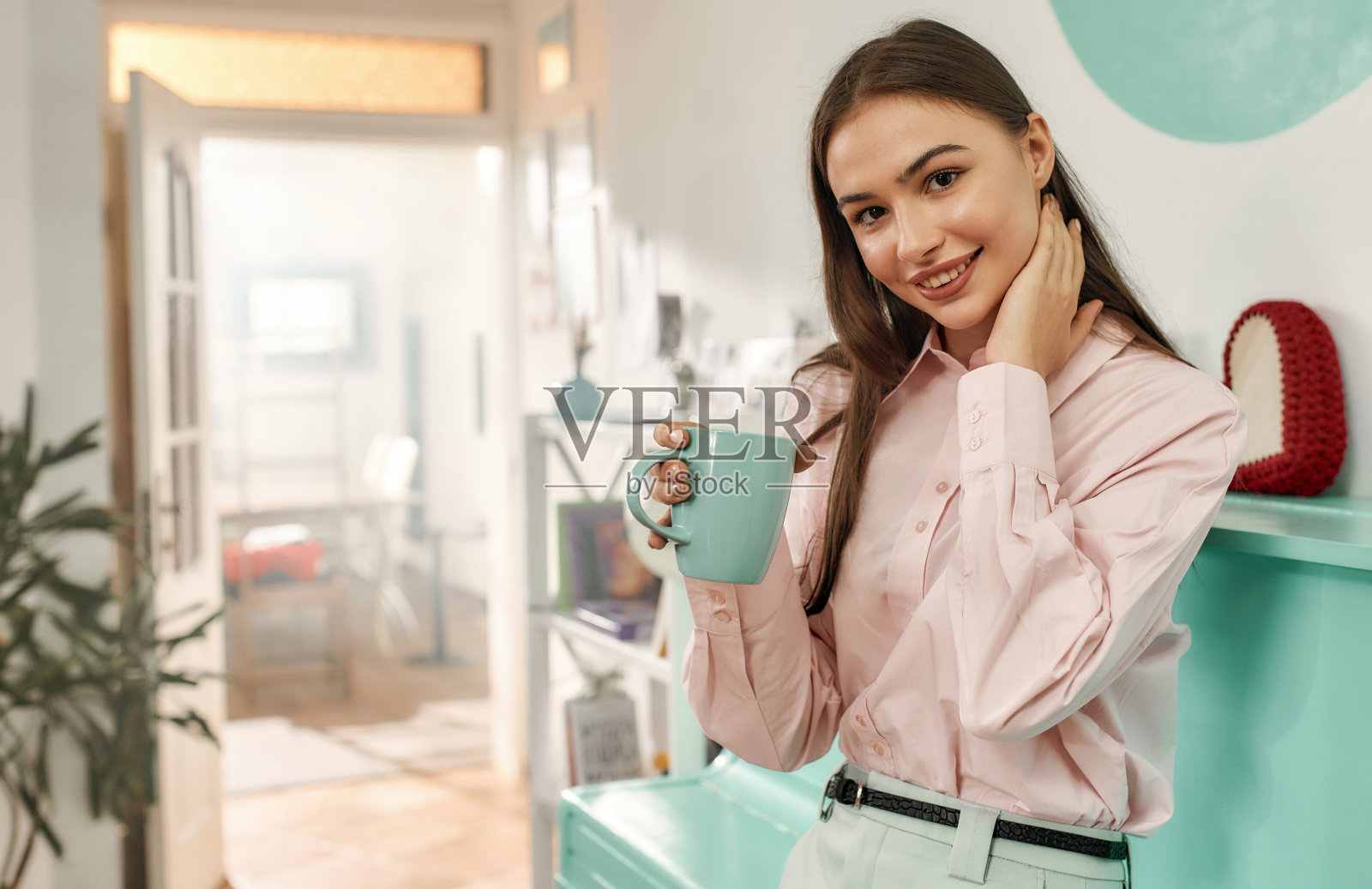 一个可爱的年轻长发褐发女人看着镜头微笑着拿着一杯茶，穿着设计师的衣服照片摄影图片