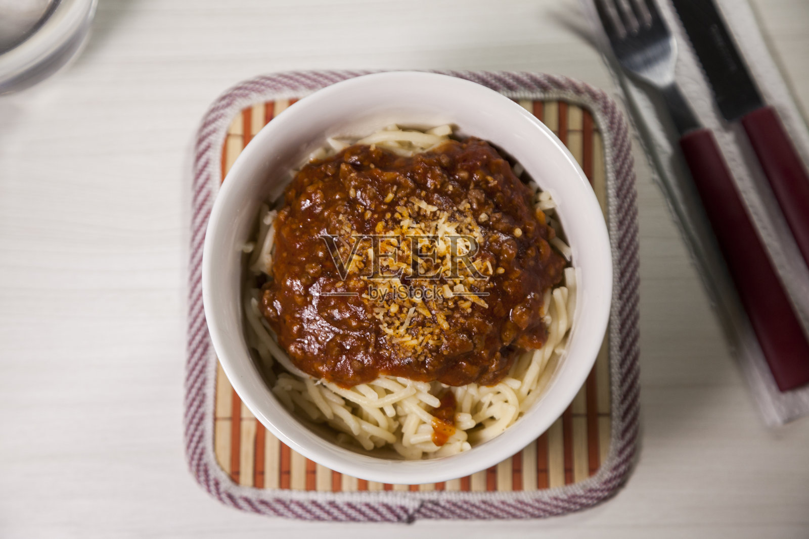 白色和蓝色的碗里有番茄酱的意大利面，白色的木质背景，旁边放着稻草盘和刀叉。照片摄影图片
