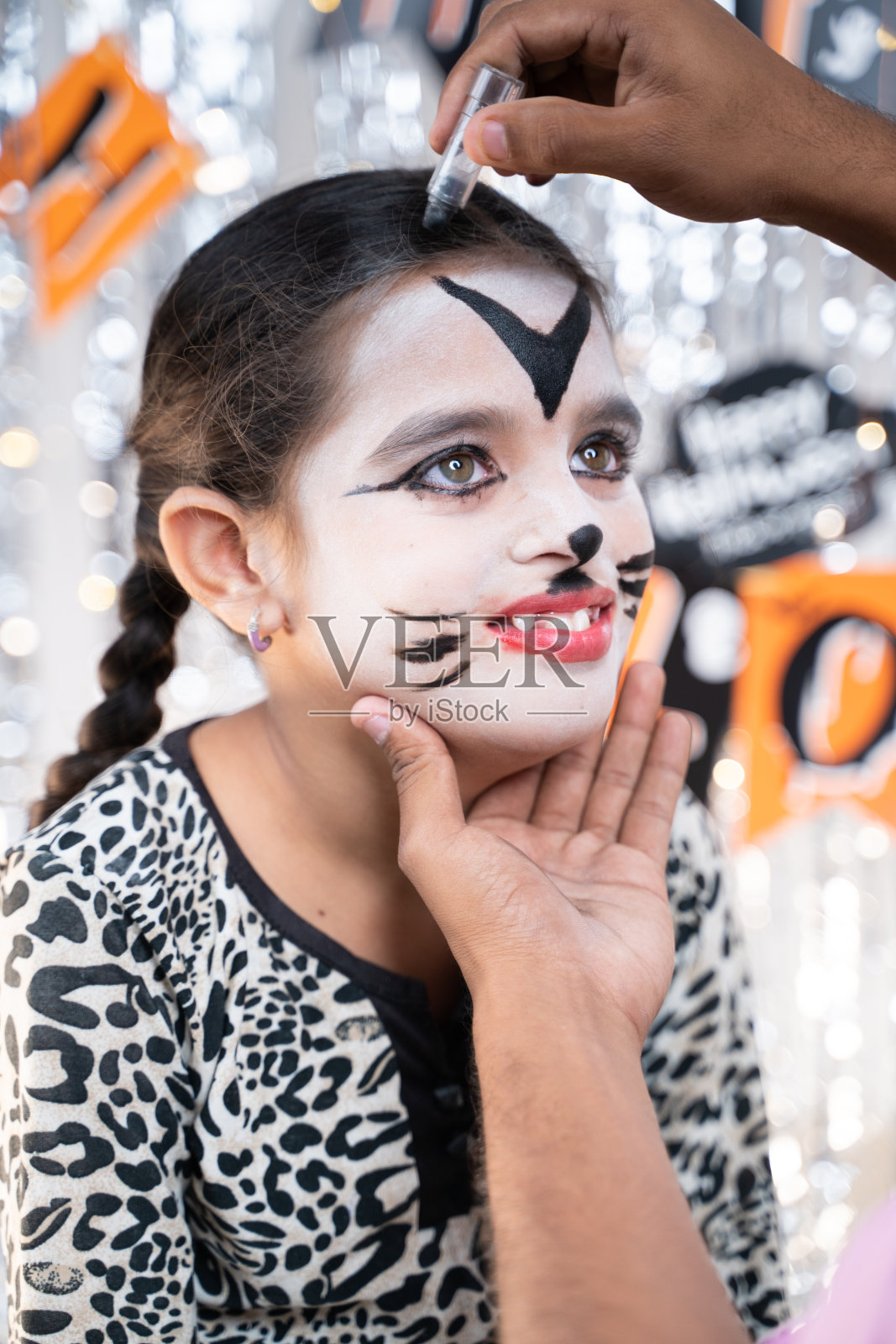 父母帮助她的女儿为万圣节化妆-万圣节的概念，节日和童年节日庆祝和准备。照片摄影图片