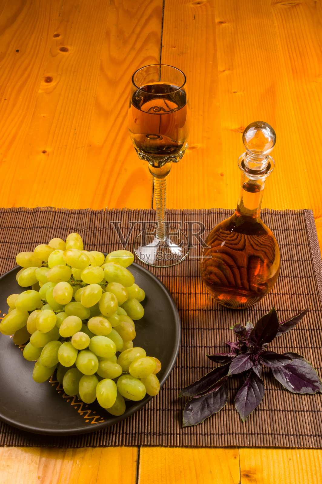 在陶瓷盘子里放一刷绿葡萄，一个醒酒器和一杯葡萄酒和奶酪照片摄影图片