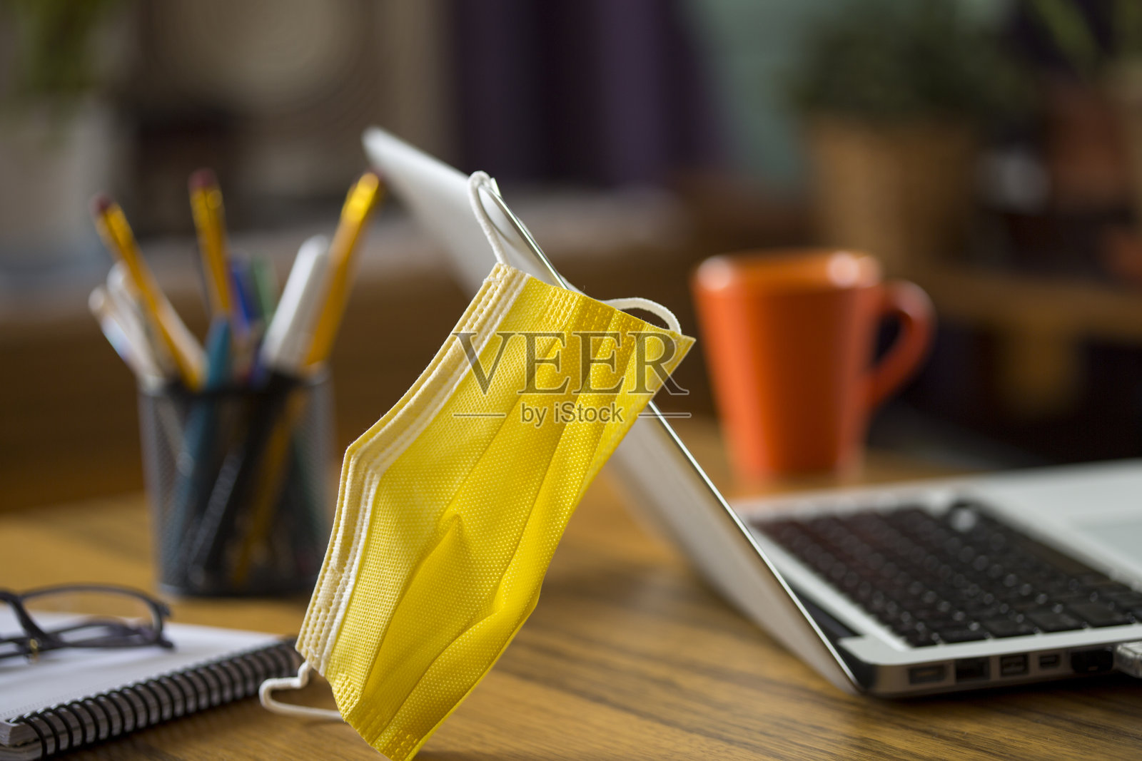 戴着医用口罩开始新的正常生活。一个黄色的保护面罩在工作台上的特写。照片摄影图片