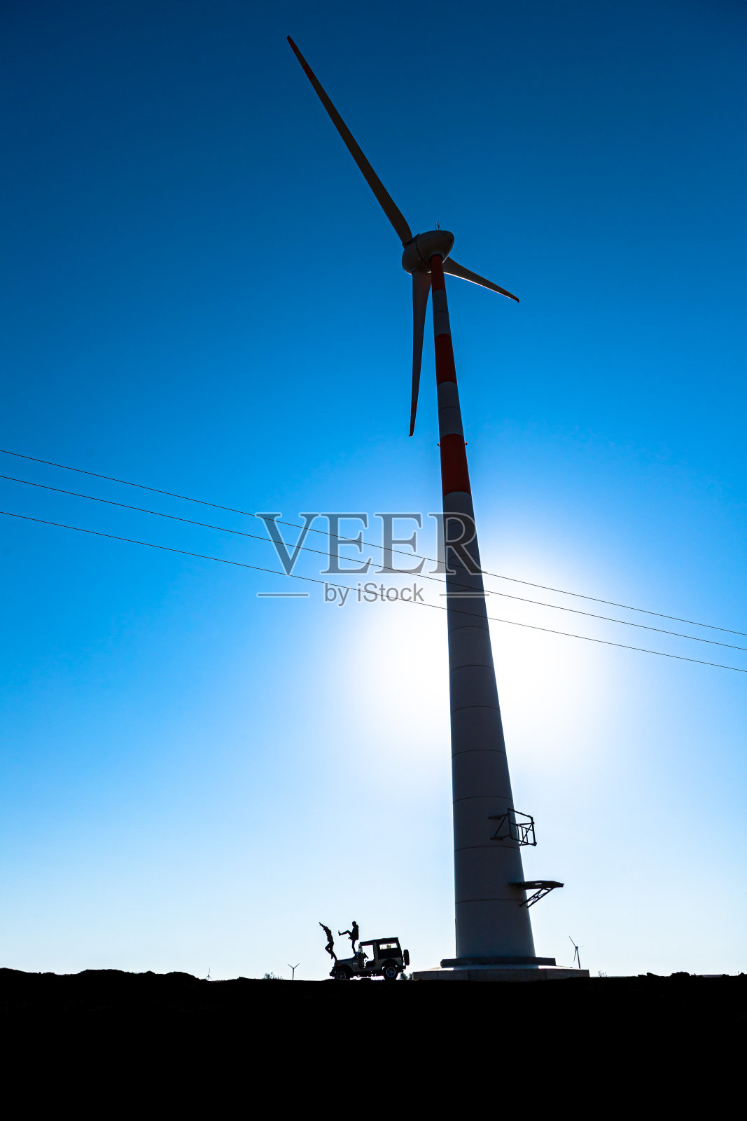两名男子从吉普车上跳下，后面是印度拉贾斯坦邦贾伊萨梅尔地区的“风车”照片摄影图片