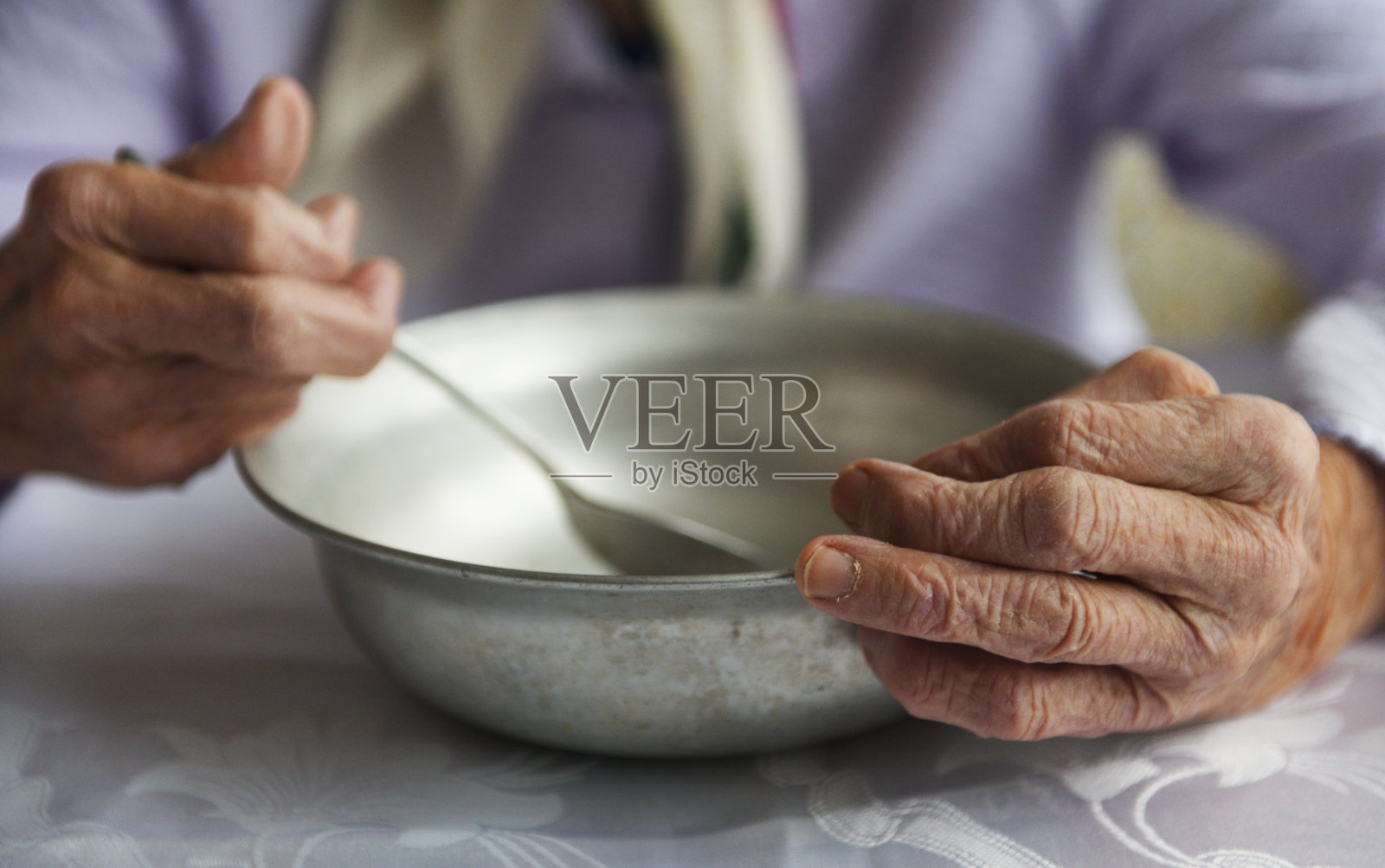 从以上观点。一个90岁的老祖母手里拿着一个空铝碗和勺子，贫穷和贫穷，老一辈人的饥饿。照片摄影图片