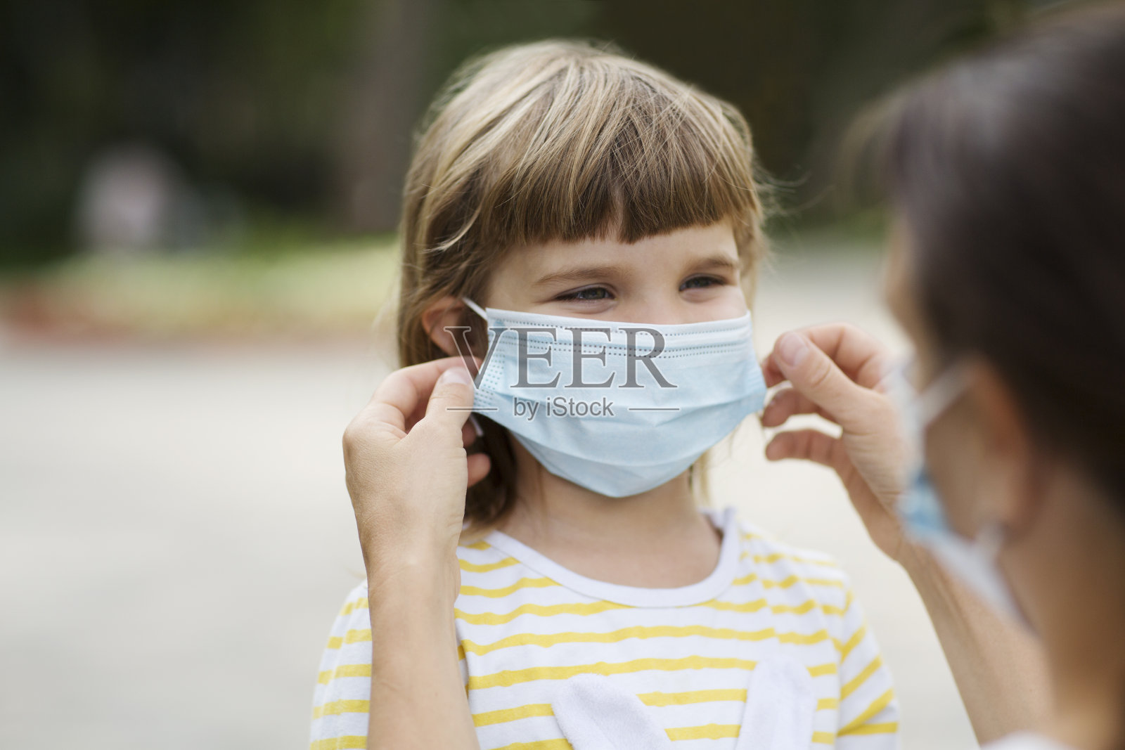 在户外，母亲戴着医用口罩给女儿戴上安全口罩。新常态本空间照片摄影图片