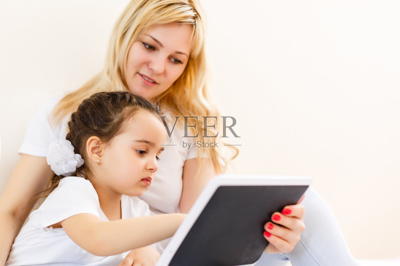 美丽的年轻女子和她迷人的小女儿躺在家里的床上微笑着使用数字平板电脑照片摄影图片