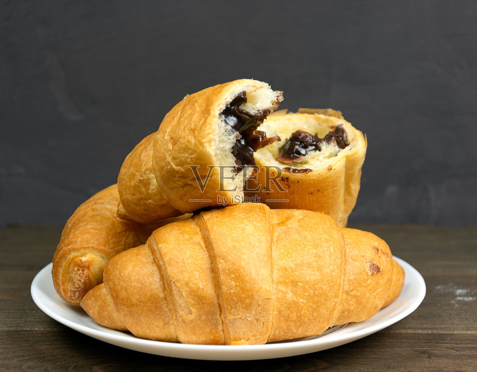 白盘子里放着巧克力羊角面包。深色背景，木桌。照片摄影图片