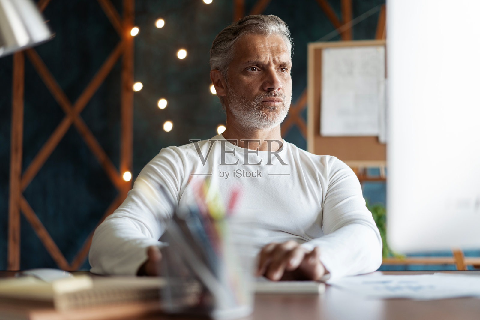 在繁忙的创意办公室里，一个灰色头发的成年人在办公桌前工作。照片摄影图片