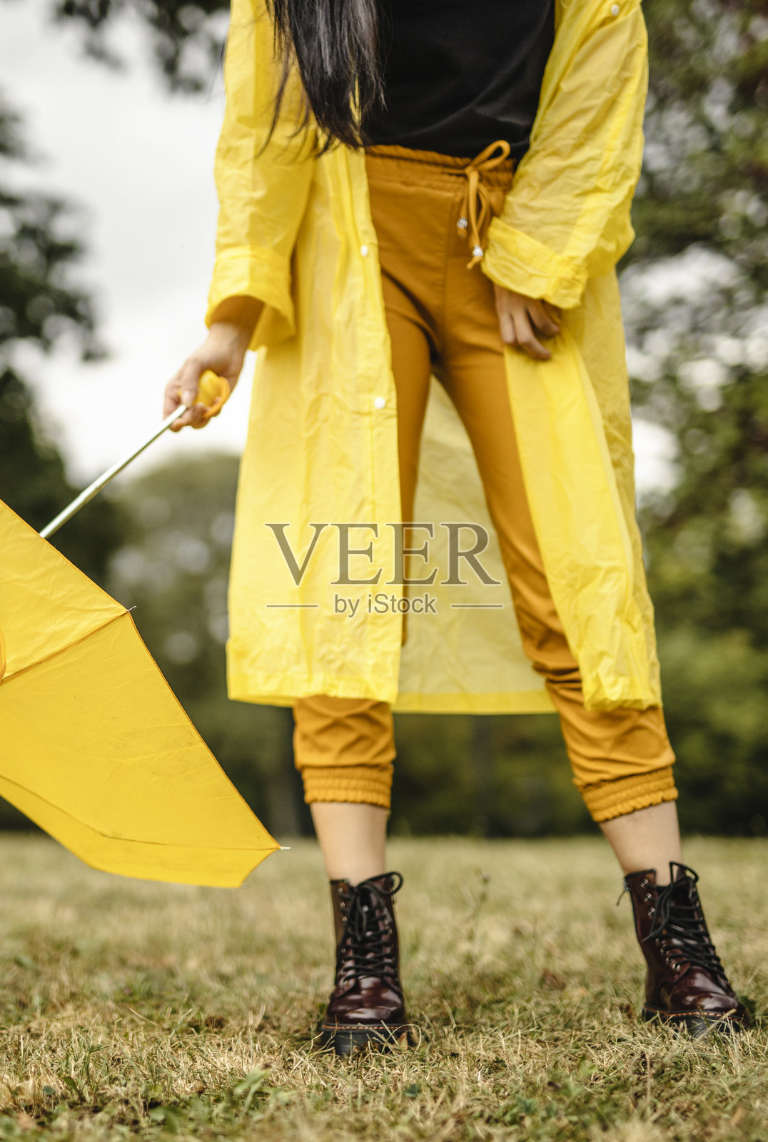 不认识的女人穿着黄色雨衣，拿着黄色雨伞，在雨天享受照片摄影图片