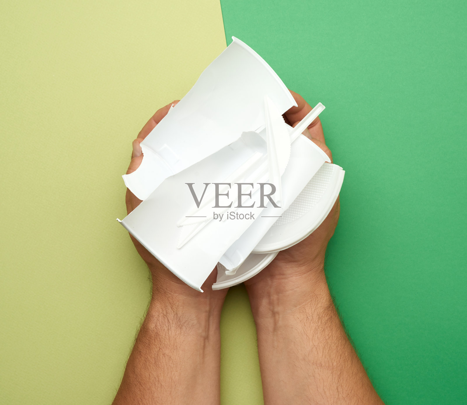 手里拿着用过的塑料盘子，一块块的塑料放在绿色的背景上照片摄影图片