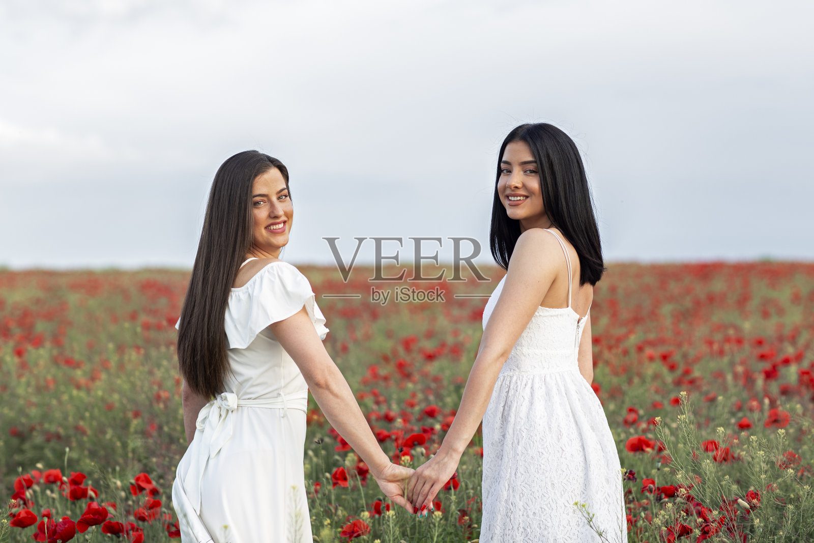 两个穿着白衣的女人站在满是鲜花的红色田野上，手牵着手照片摄影图片