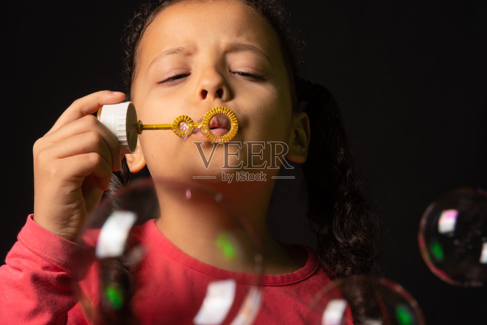 巴西女孩与粉红色的顶部玩肥皂泡，低调的肖像，黑色背景，选择性焦点。照片摄影图片