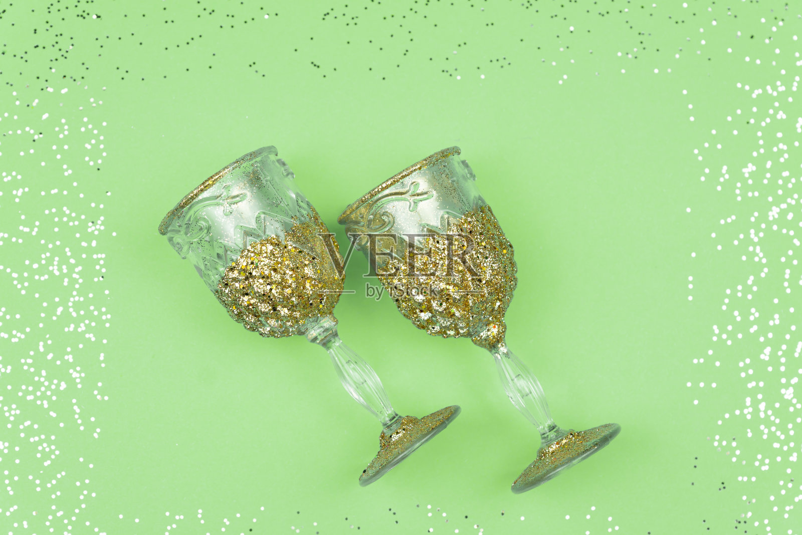 两个空的香槟酒杯在绿色闪闪发光的背景上。五彩纸屑装饰的节日贺卡照片摄影图片