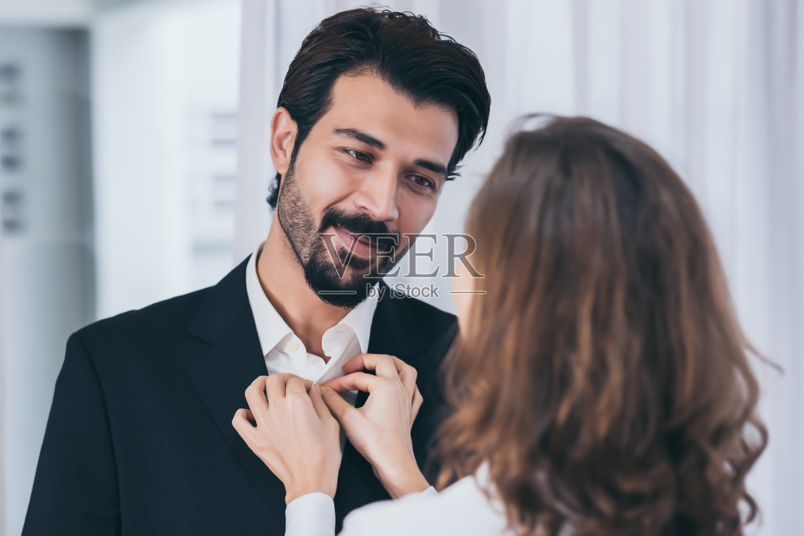 英俊的商人看着心爱的妻子为他整理衬衫照片摄影图片