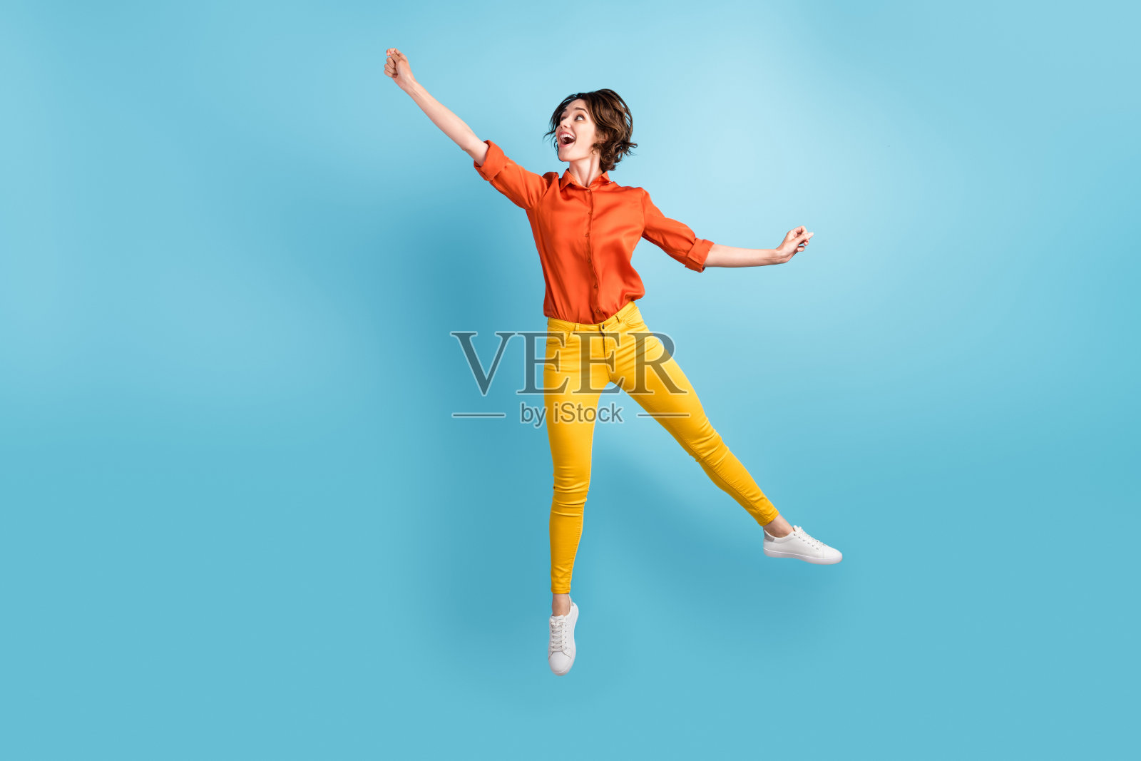 迷人的有趣的女士的全身照片跳高飞行上升空气想象的伞快乐的周末穿橙色的衬衫黄色的裤子运动鞋孤立的蓝色背景照片摄影图片