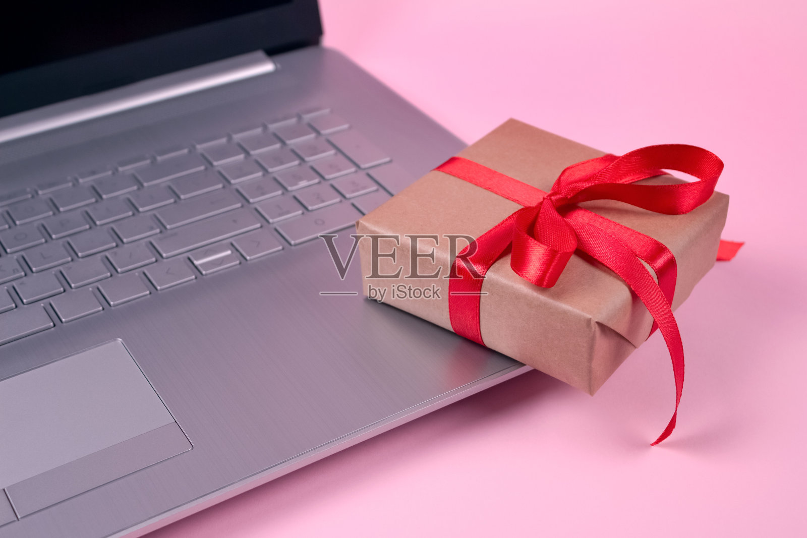 前视图在笔记本电脑和礼物盒与红色蝴蝶结在粉红色的背景与copyspace为您的文本。季节性促销，黑色星期五和网络星期一的概念。网上购物照片摄影图片