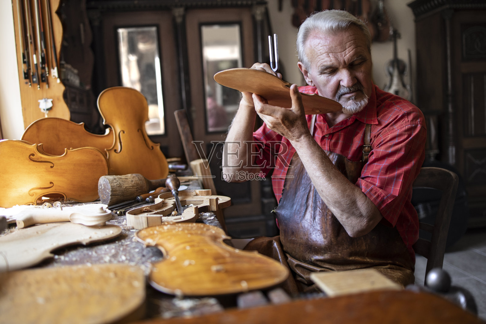 艺术和工艺品。高级木匠工匠在他的老式木匠作坊检查木材的质量。在背景硬木小提琴零件和工具。照片摄影图片