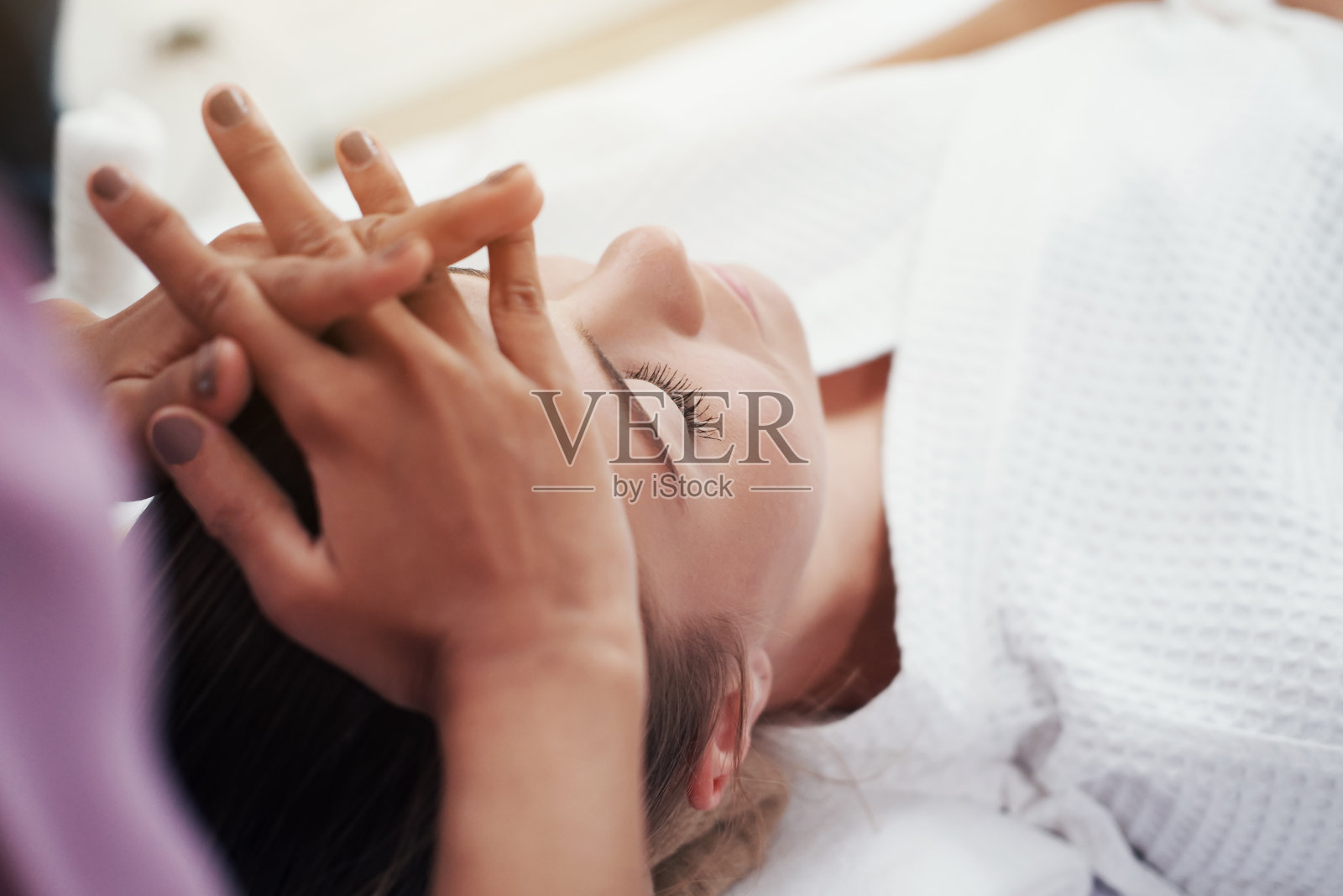 闭合的亚洲按摩治疗师女人的手正在做传统的头部和面部治疗按摩白种人女性是躺在床上的替代医学治疗水疗中心在泰国。照片摄影图片