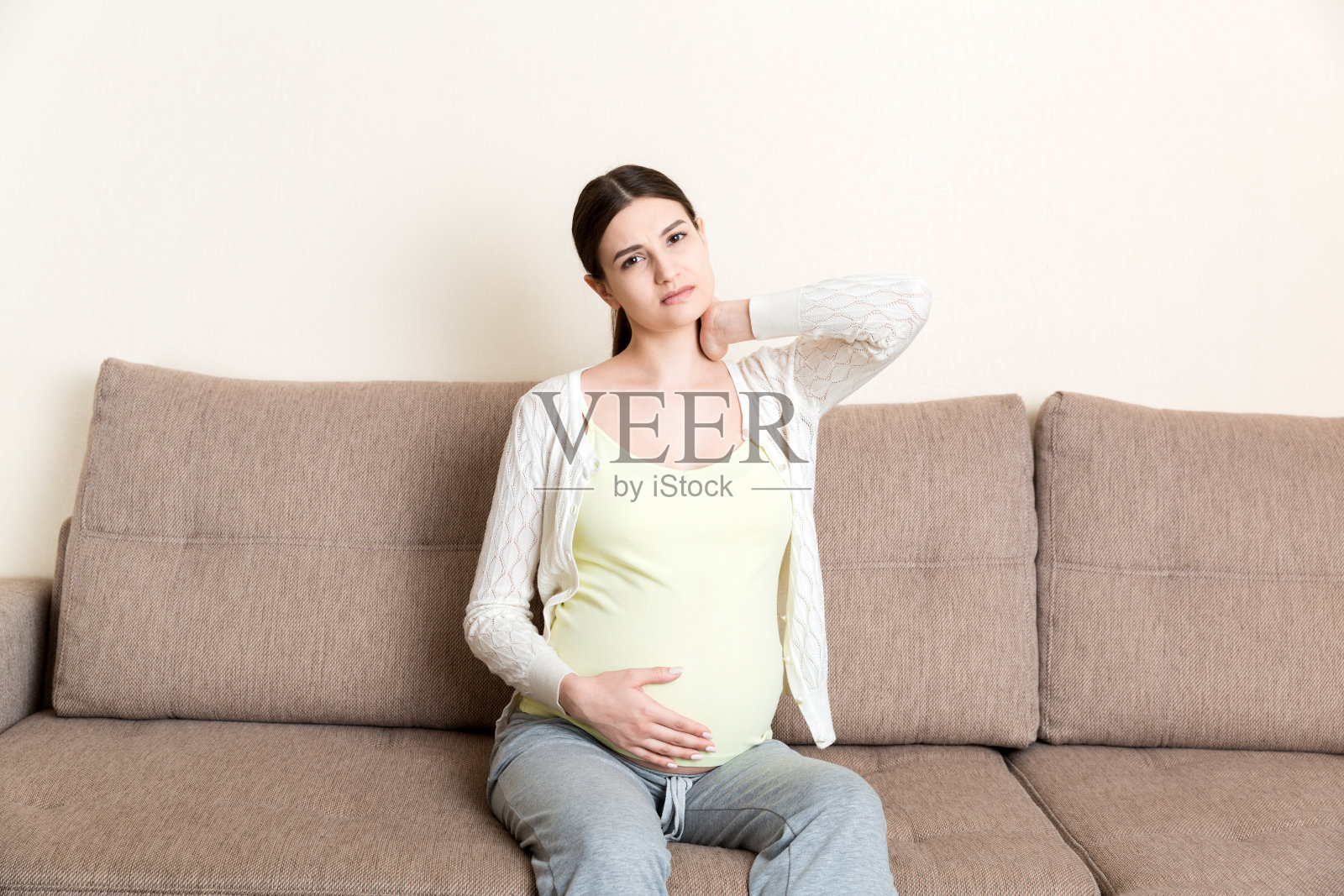 年轻孕妇头痛坐在沙发上。怀孕期望概念照片摄影图片