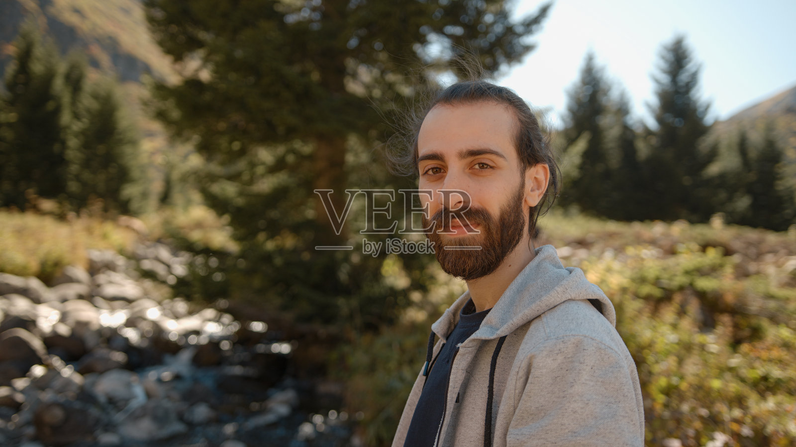 一个年轻的嬉皮士站在小溪边看着镜头微笑着照片摄影图片