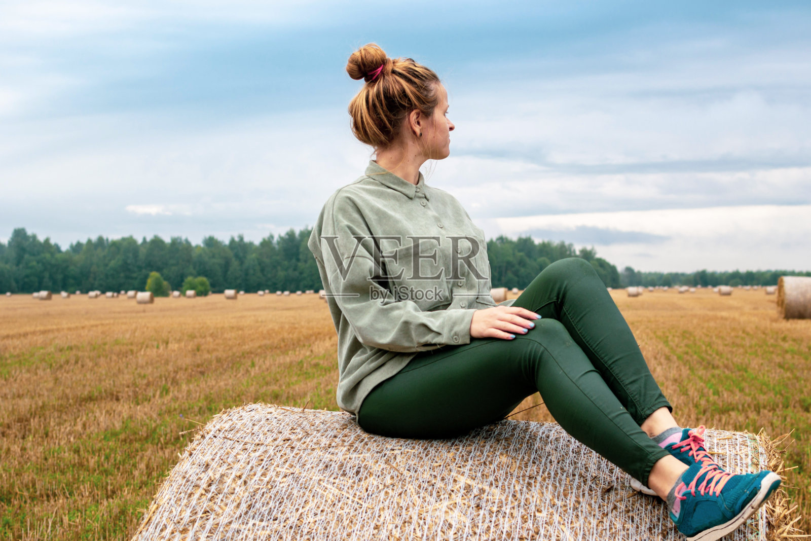 一个年轻女子在农地的圆捆干草上休息照片摄影图片