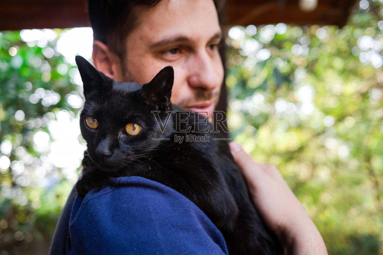 肩上抱着一只可爱的黑猫的男人照片摄影图片