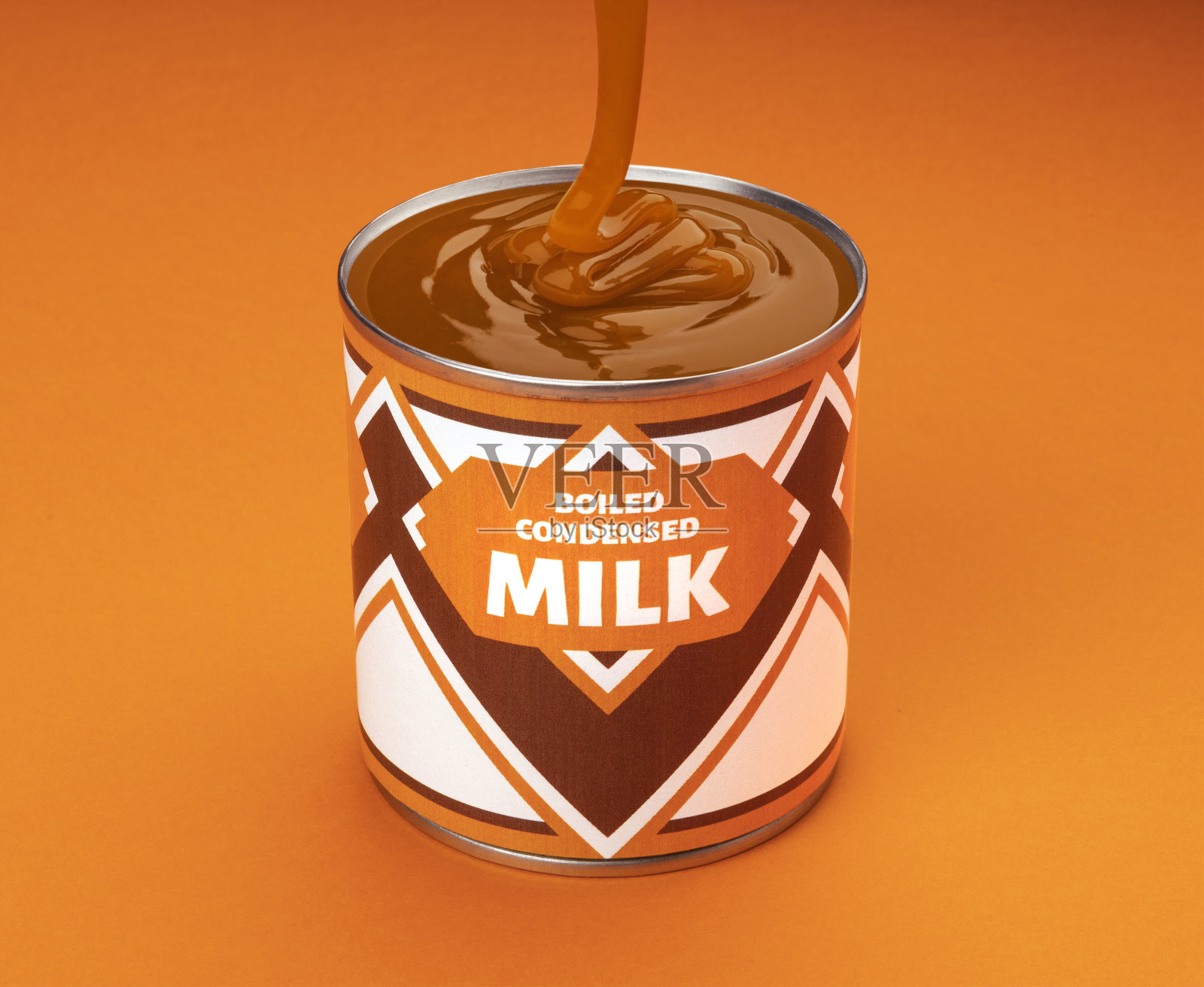 将煮沸的炼乳流进橘色背景的罐子里照片摄影图片