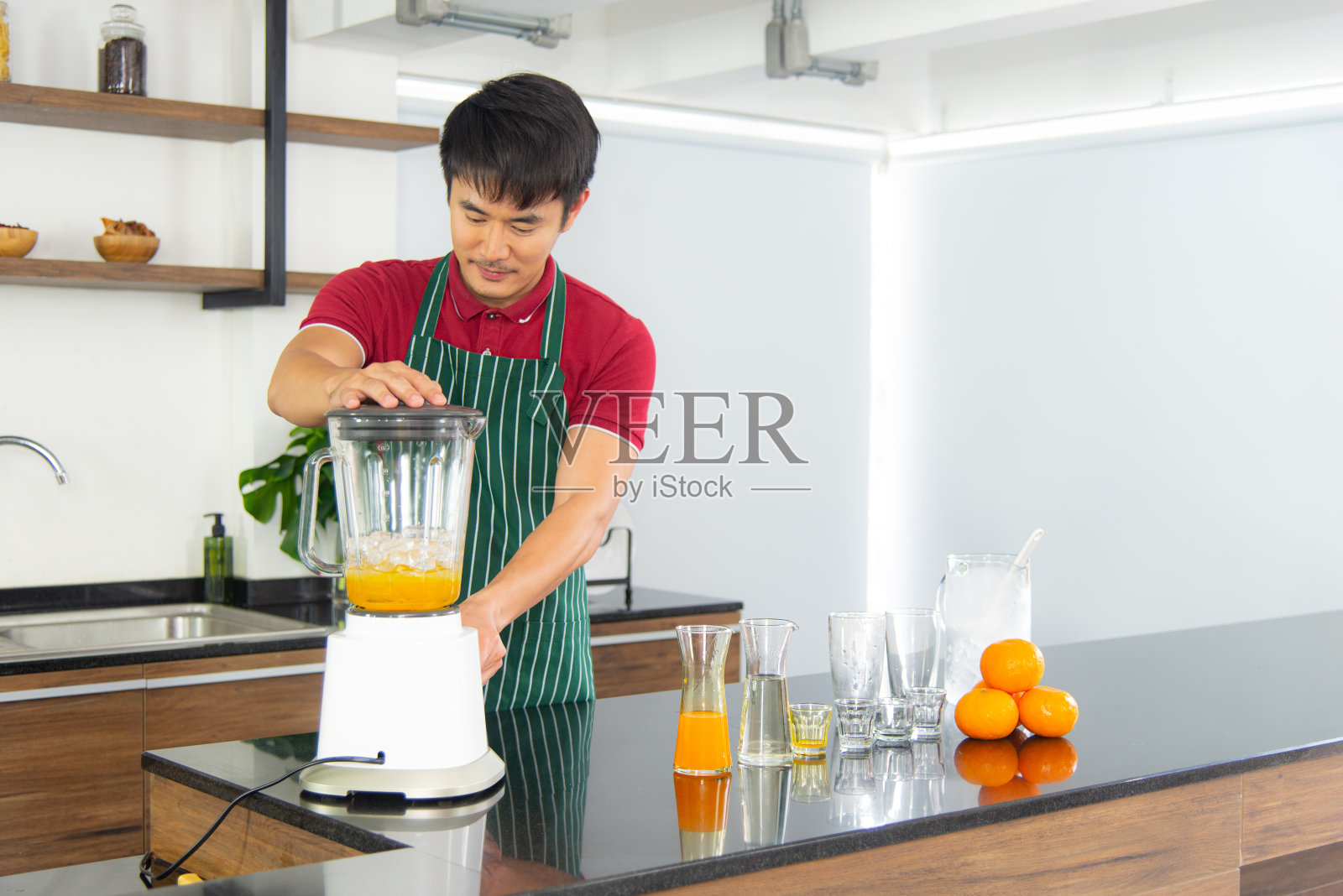 肖像聪明和英俊的亚洲男子准备健康的膳食和新鲜的有机橙汁在阁楼风格的厨房。照片摄影图片