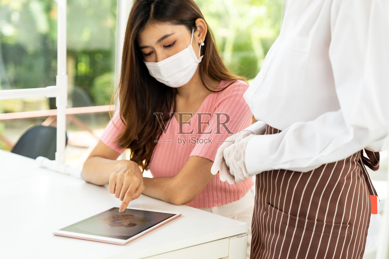 亚洲女服务员用平板电脑向顾客展示菜单。照片摄影图片