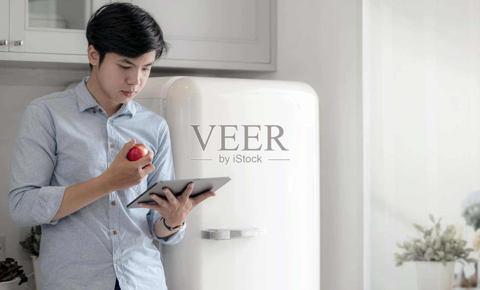 一个年轻人周末站在家里厨房里用平板电脑。照片摄影图片