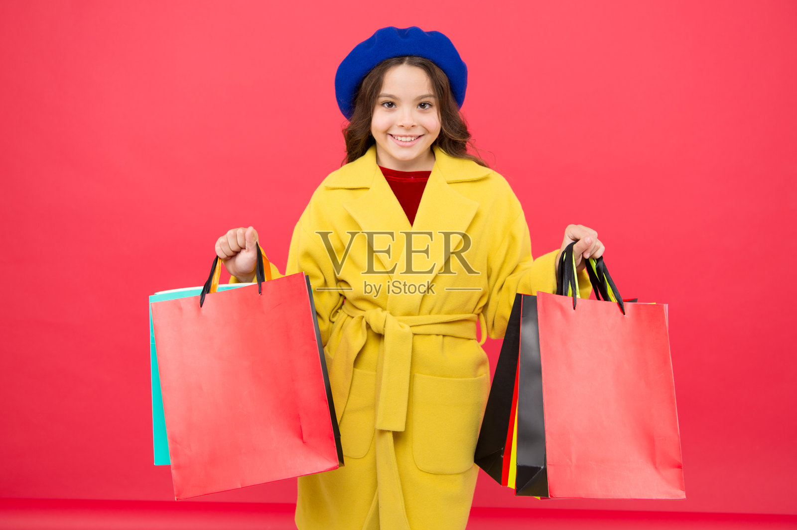时尚达人喜欢购物。沉迷于购物。通过商店的春季销售，让主要的衣柜焕然一新。女孩可爱的孩子拿着购物袋红色的背景。在生日假期打折购物照片摄影图片