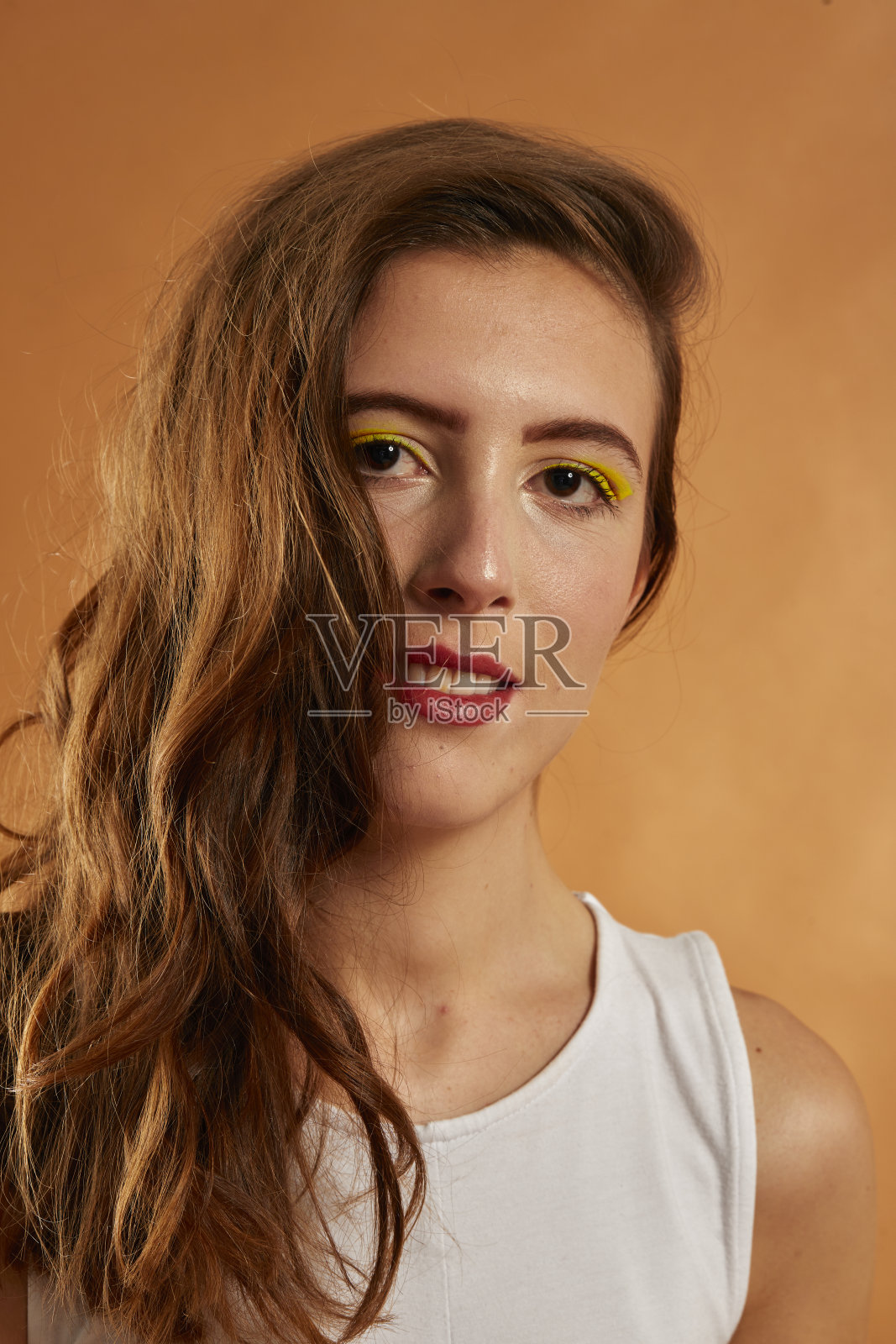 年轻的西班牙女人身穿牛仔裤和白色紧身上衣，棕色背景的运动鞋照片摄影图片