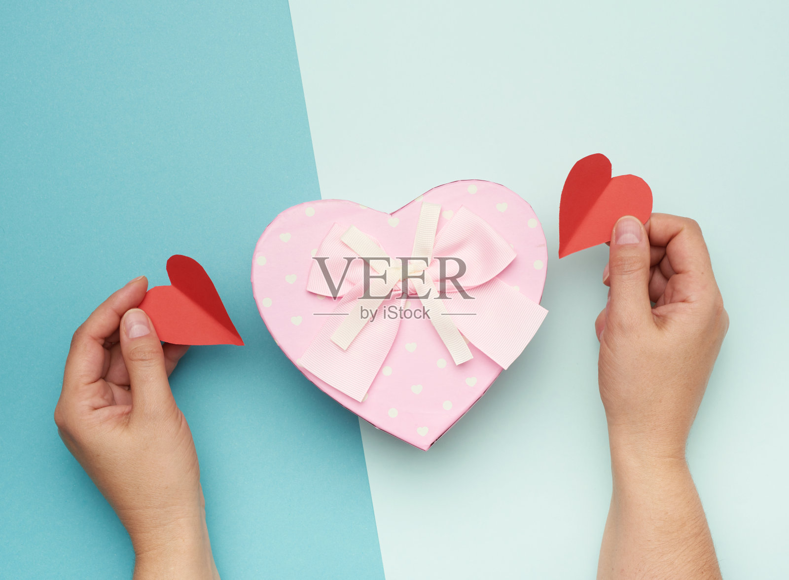 双手拿着一个蓝色背景上带蝴蝶结的粉色纸盒照片摄影图片