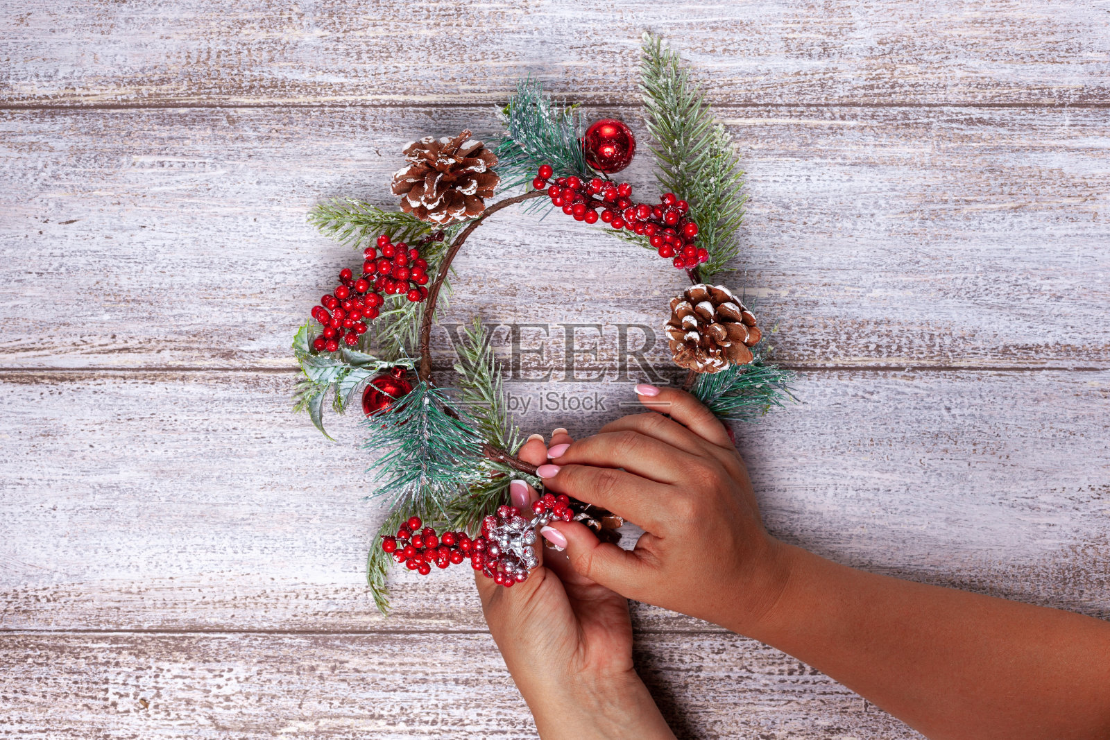 女人的手用冷杉树枝、松果和红色浆果在木头背景上制作了一个圣诞花环照片摄影图片