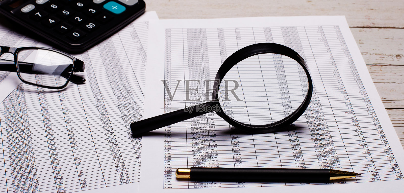 桌面上有一个放大镜、报告、计算器、眼镜和一支笔。工作场所的关闭照片摄影图片