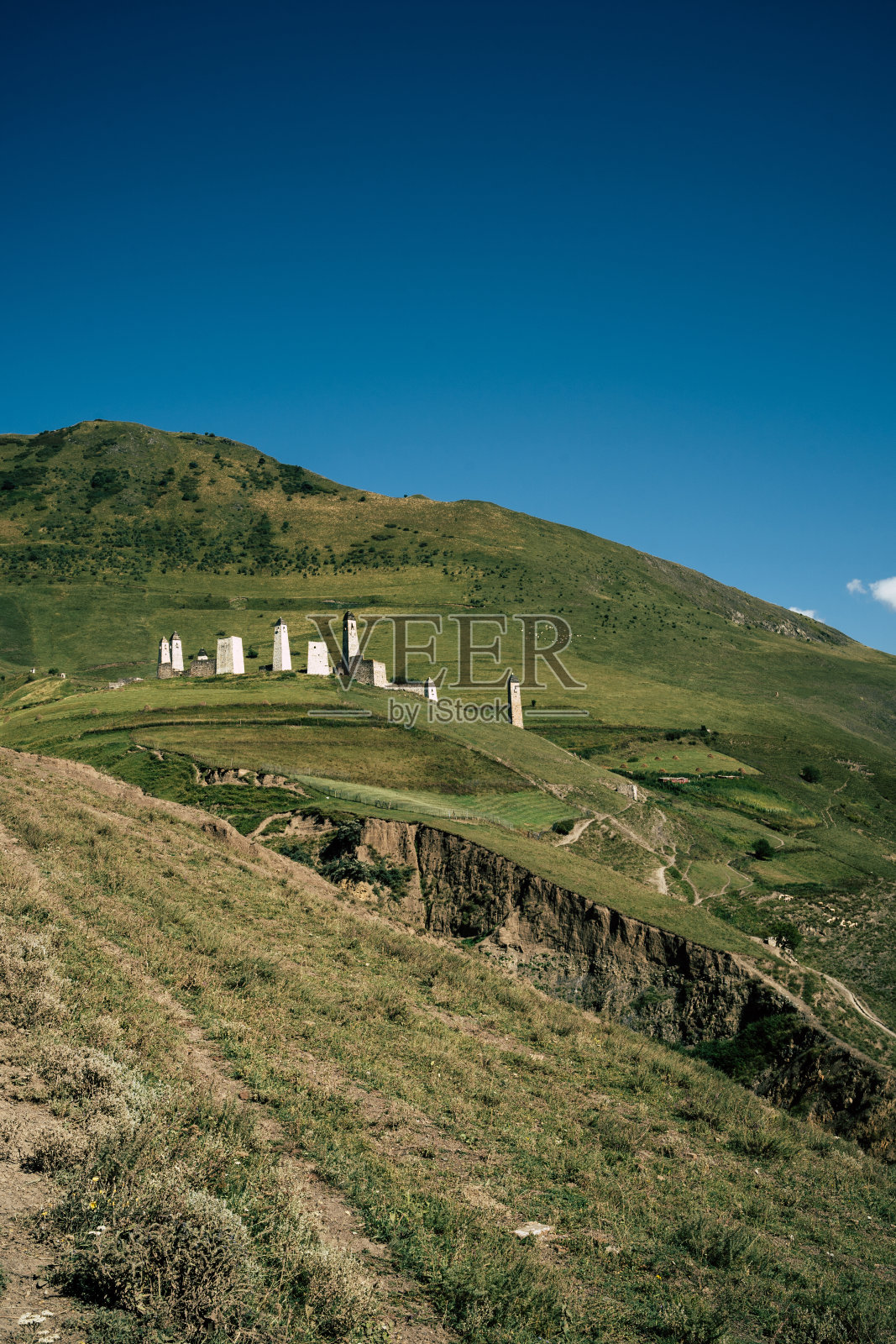 古老的石塔在绿色的山区地形。在夏季的日子里，古镇的古老石砌建筑坐落在绿树成荫的小山上，群山被森林和雾所覆盖照片摄影图片