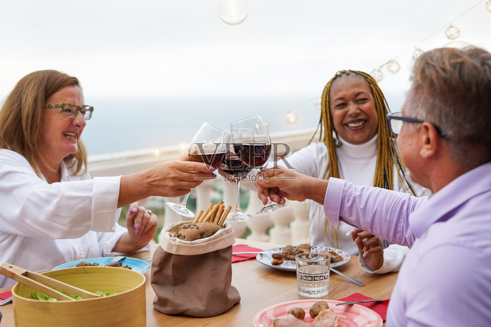 快乐的多民族老年人一起享受户外晚餐和红酒欢呼照片摄影图片