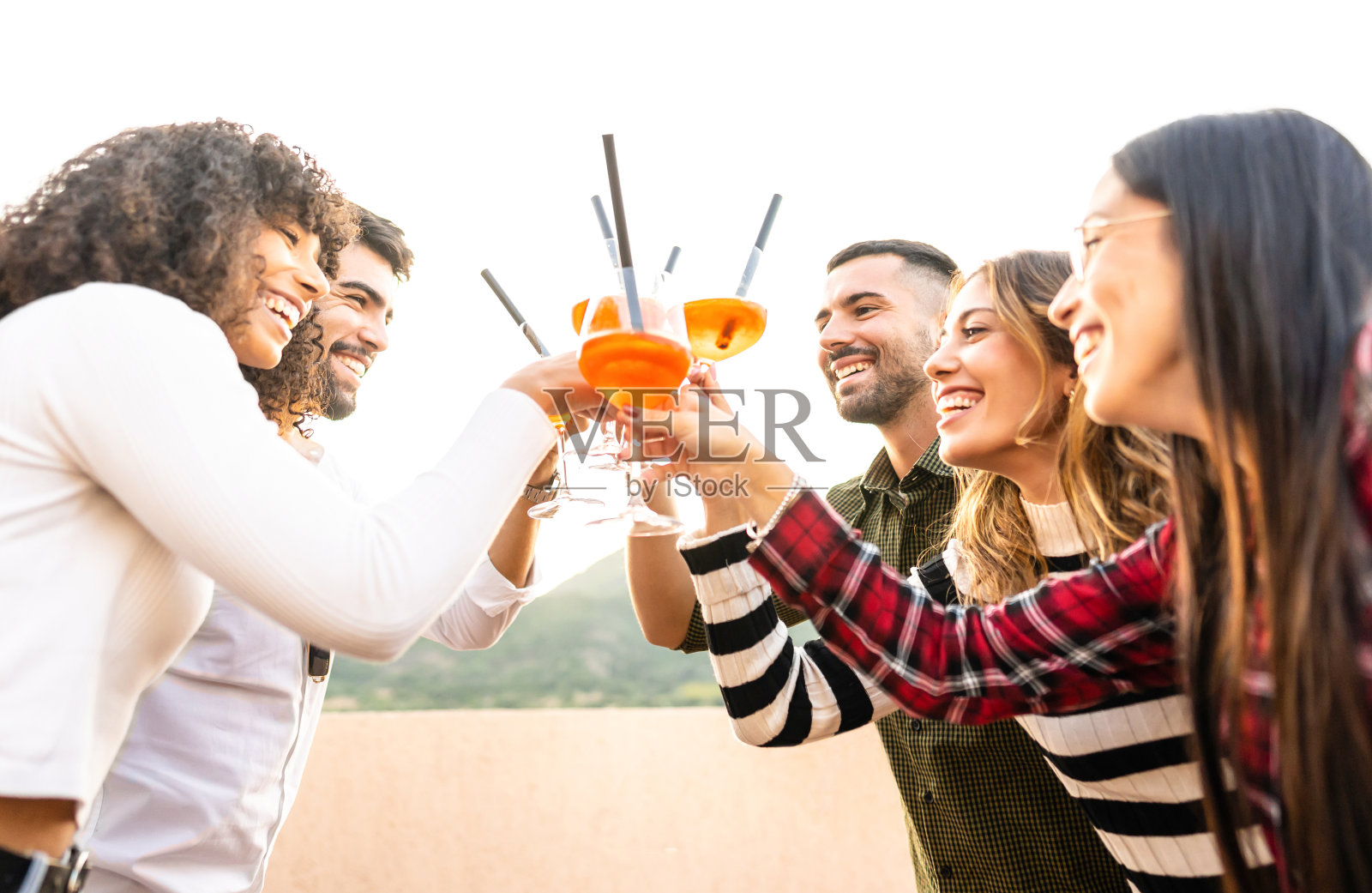 混合种族快乐的朋友群在日落室外与喷雾器杯敬酒-年轻人有乐趣一起喝鸡尾酒的开胃酒时间-明亮生动的滤镜与焦点在胡子男人照片摄影图片