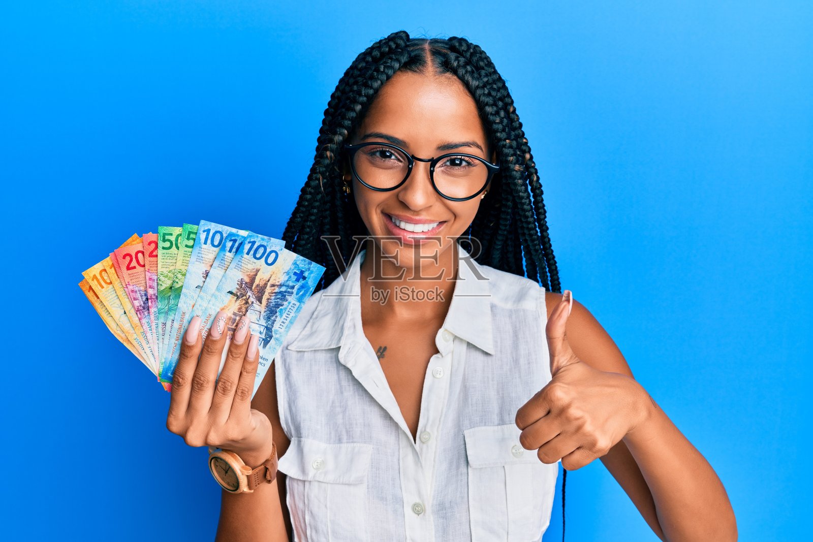 美丽的西班牙妇女持有瑞士法郎钞票微笑快乐和积极，大拇指做优秀和批准的标志照片摄影图片