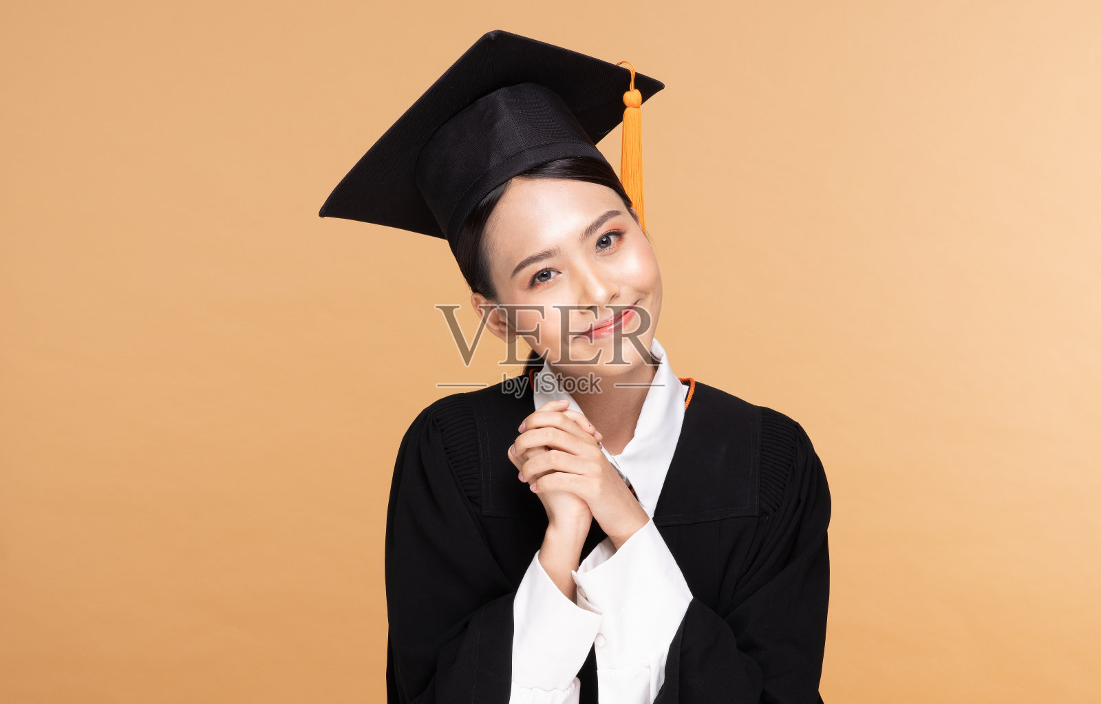 美丽迷人的亚洲女人毕业在帽子和长袍微笑如此骄傲和幸福，孤立在米色背景，教育成功的理念照片摄影图片